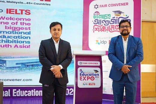 Two partners in suits posed on the branded IELTS/BIEE stage backdrop