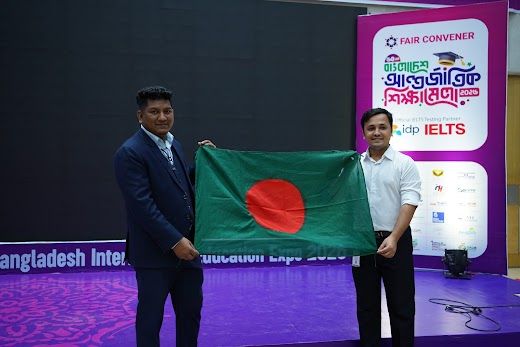 Two men holding the Bangladesh national flag beside the Fair Convener stand